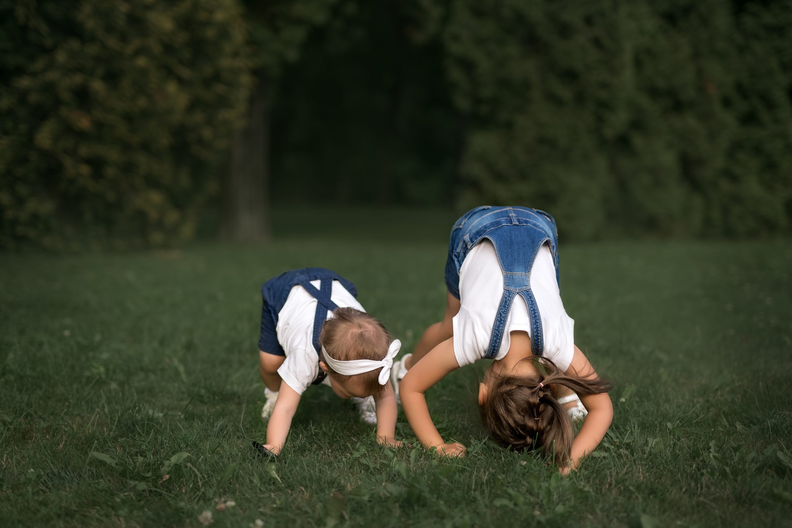 Two little baby girls play on the grass and have fun. Girls stand on their heads