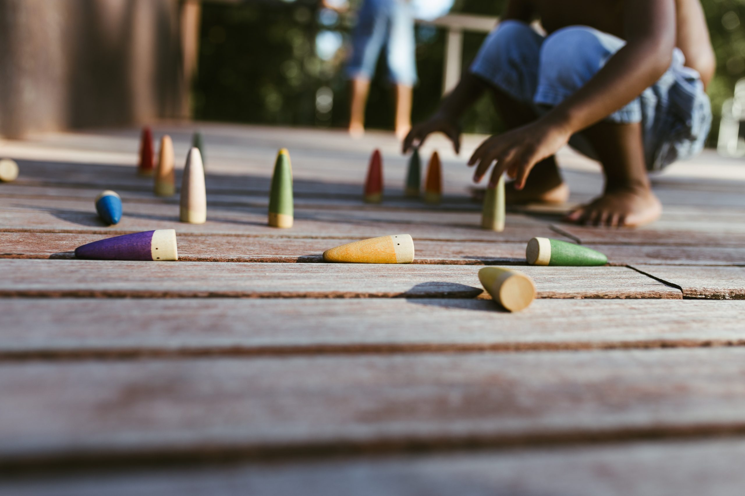 Unrecognizable shirtless African American boy sitting on wooden surface and playing with colorful cones on sunny day